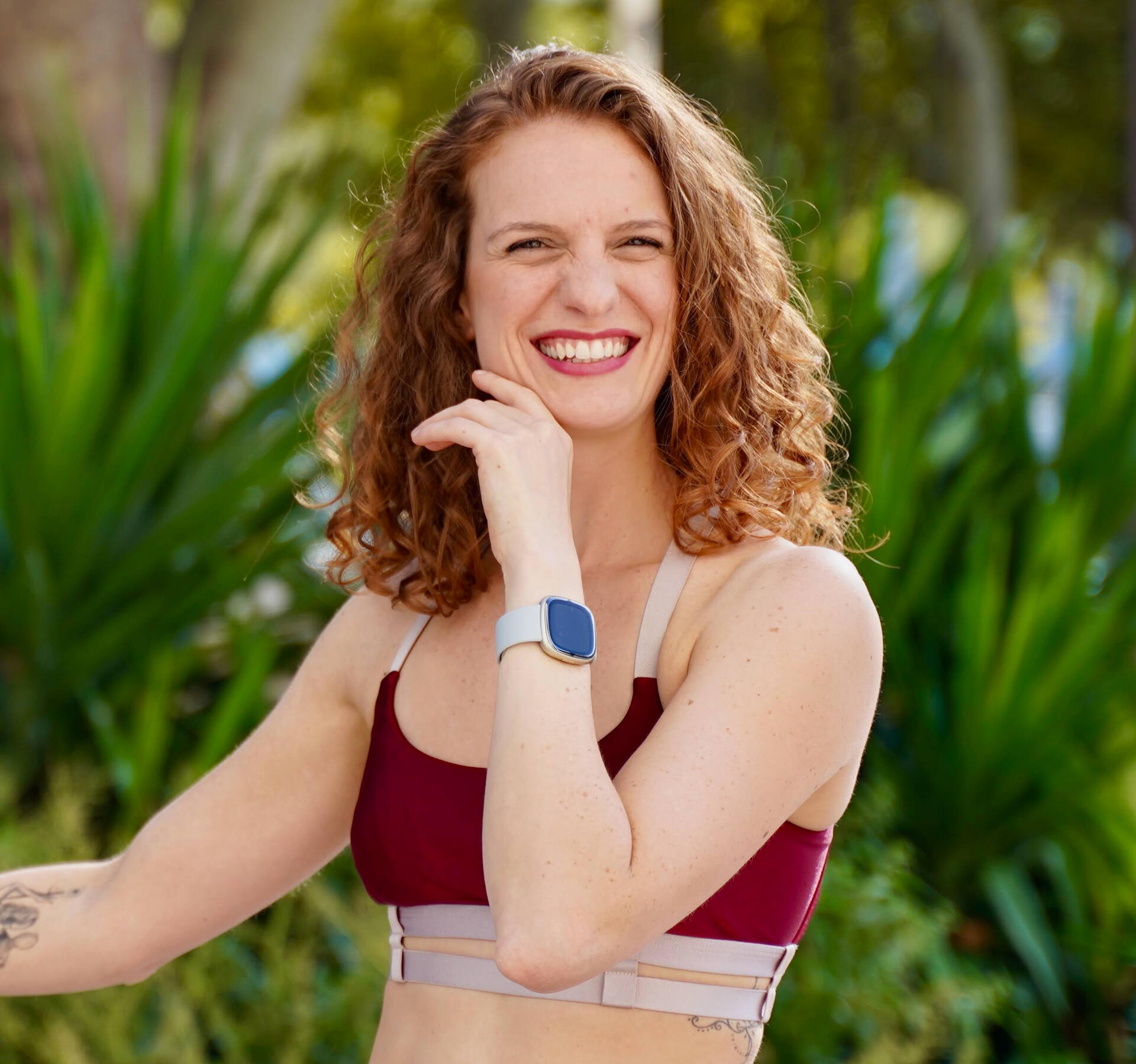 Camila smiling in a red top and leafy background